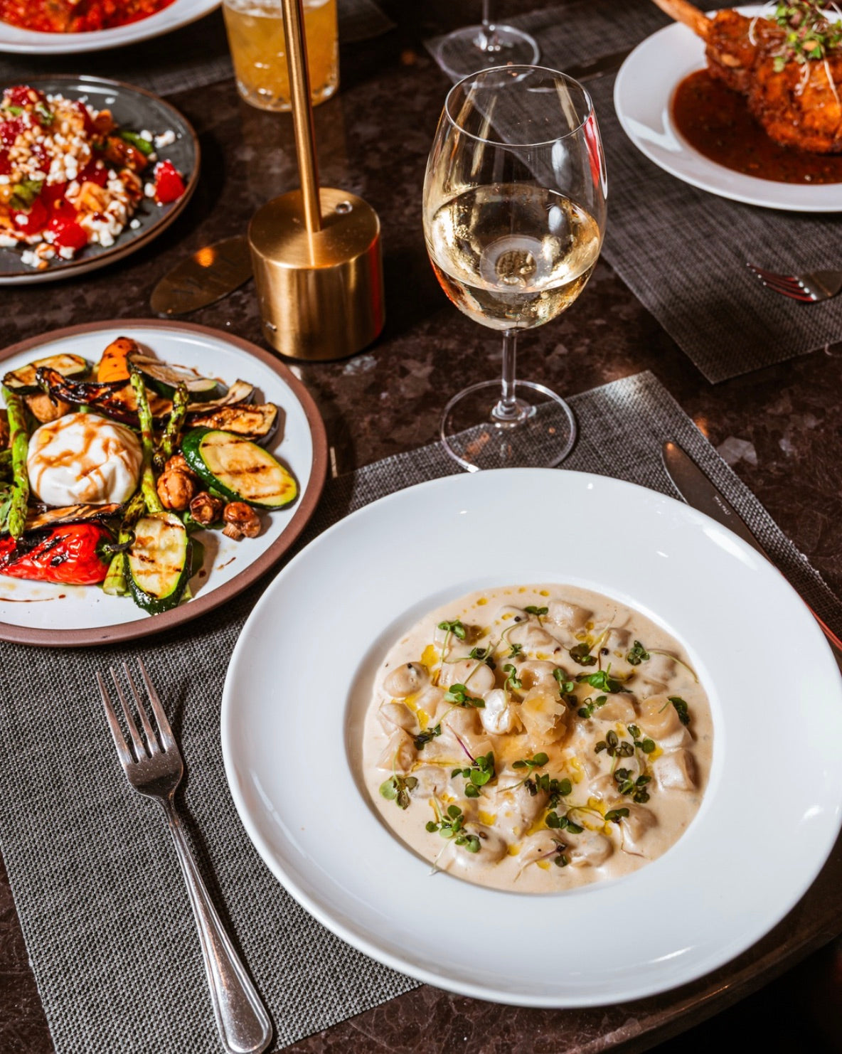 Table de marbre éclairée à la chandelle — gnocchis crémeux, lampe dorée et vin blanc